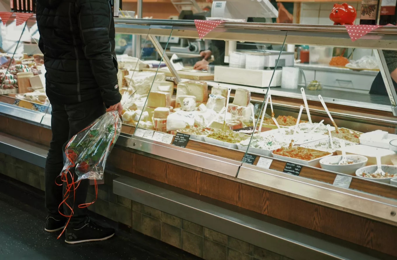 Un homme avec un bouquet de roses se tient devant la vitrine d'un crémier / fromager