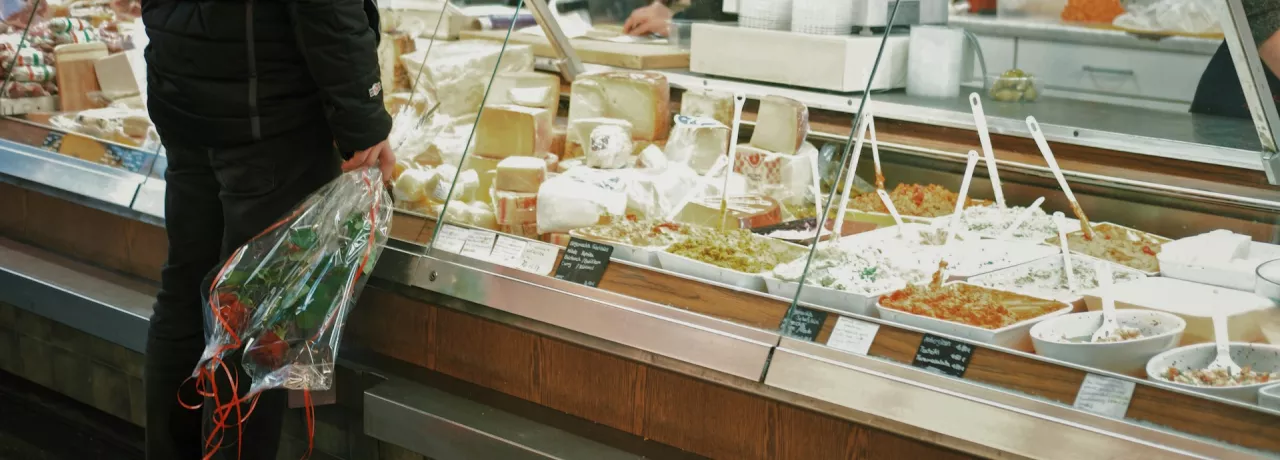 Un homme avec un bouquet de roses se tient devant la vitrine d'un crémier / fromager