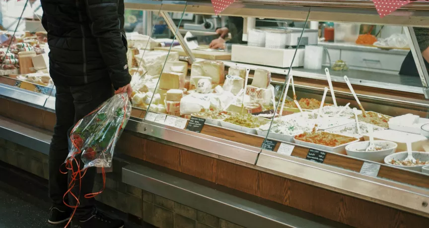 Un homme avec un bouquet de roses se tient devant la vitrine d'un crémier / fromager