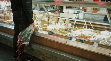 Un homme avec un bouquet de roses se tient devant la vitrine d'un crémier / fromager
